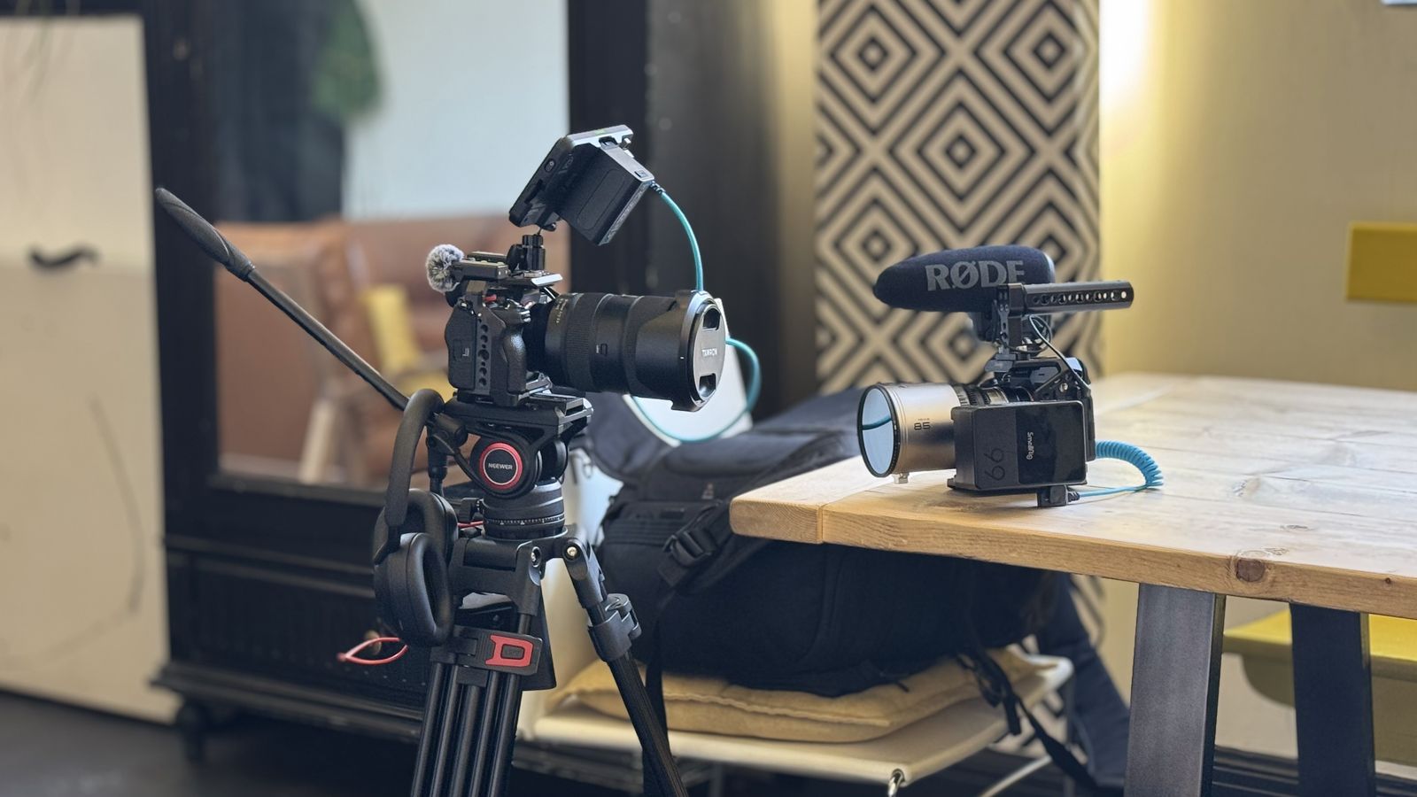 Two cameras set up for filming indoors, one on a tripod and one on a table with a mounted microphone.