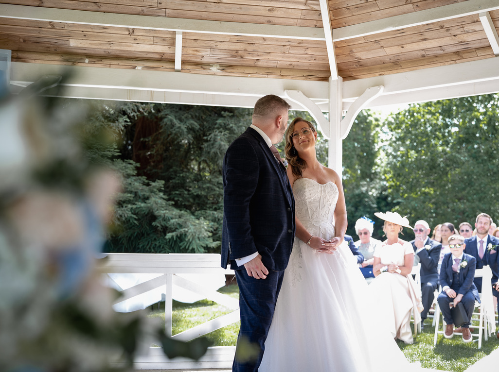 A bride and groom face each other during their outdoor wedding ceremony, with guests seated behind them.